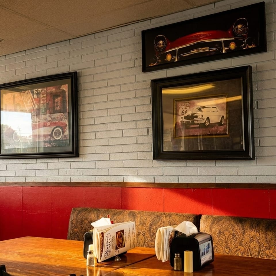 Cozy restaurant booth with wooden tables, red wall paneling, vintage automobile artwork, and tabletop menus and condiments.