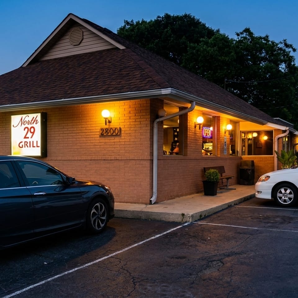 North 29 Grill restaurant exterior glowing at dusk, with brick walls, entrance, signage, and parked cars.