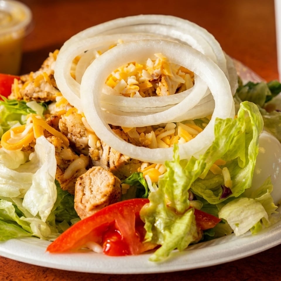 Plate of chopped salad with grilled chicken, shredded cheese, onion rings, lettuce, tomatoes, dressing, and a drink.